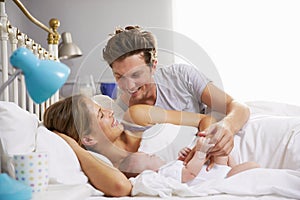 Family In Bed Holding Sleeping Newborn Baby Daughter