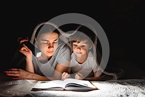 Family bedtime. Mom and children son are reading a book on bed. Pretty young mother and lovely boy having fun in children room