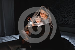 Family bedtime. Mom and children son are reading a book on bed. Pretty young mother and lovely boy having fun in children room