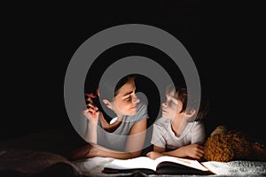 Family bedtime. Mom and children son are reading a book on bed. Pretty young mother and lovely boy having fun in children room