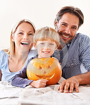 A family behing their jack-o-lantern. Portrait of a husband and a wife with their son behind a carved pumpkin for