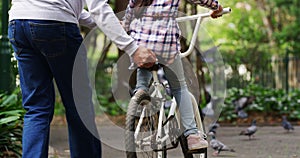 Family, bike and a girl learning to ride in a park with the hand of a grandparent closeup outdoor for development. Back