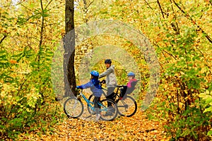 Family on bikes in autumn park, father and kids cycling