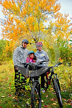 Family on bikes in autumn park, parents and kid cycling