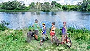 Family on bikes cycling outdoors, active parents and kids on bicycles, aerial top view of happy family with children near river