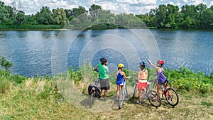 Family on bikes cycling outdoors, active parents and kids on bicycles, aerial view of happy family with children relaxing