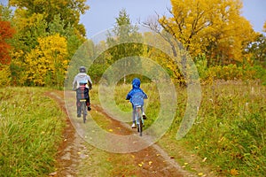 Family on bikes in golden autumn park, father and kids cycling on trail, active sport with children