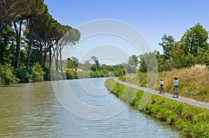 Family on bikes, mother and daughter cycling by canal du Midi, summer vacation in France