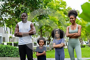 A family of black Americans and their son and daughter in sportswear line up to take pictures, smiling cheerfully at the camera