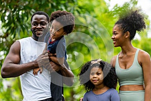 A family of black Americans and their son and daughter in sportswear line up to take pictures, smiling cheerfully at the camera