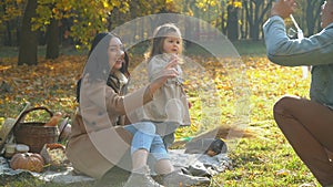 Family blowing air bubbles. Mother and father with daughter having fun outdoor. Picnic in the autumn park