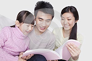 Family bonding together, smiling and reading on the sofa, looking down at book, studio shot photo