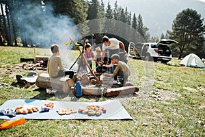 Family bonfire in mountain. Frying sausages. Four kids camping. Autumn hike and camp weather. Warming and cooking near flame