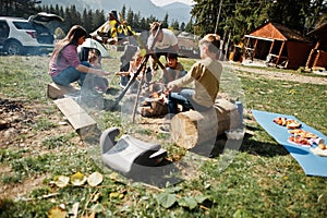 Family bonfire in mountain. Frying sausages. Four kids camping. Autumn hike and camp weather. Warming and cooking near flame