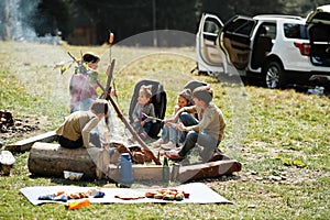 Family bonfire in mountain. Frying sausages. Mother with four kids camping. Autumn hike and camp weather. Warming and cooking near