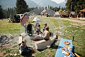 Family bonfire in mountain. Mother with four kids camping. Autumn hike and camp weather. Warming and cooking near flame together