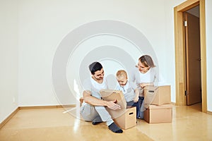 Family with boy unpacking moving cardboard boxes at new home