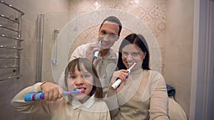 Family brushing teeth, lovely little girl with parents with toothbrush brushing teeth in front of mirror