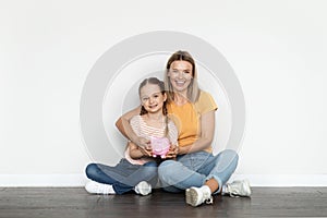 Family Budget. Smiling Beautiful Mother And Little Daughter Holding Piggy Bank