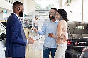Family Buying Car. African American Spouses Purchasing New Vehicle In Dealership Center