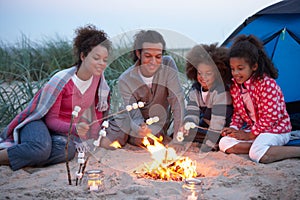 Family Camping On Beach And Toasting Marshmallows