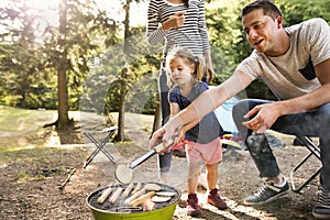 Family camping in forest, cooking meat on barbecue grill.