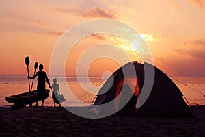 Family camping and kayaking on the beach with red sky sunset.