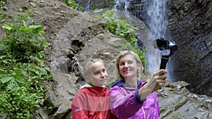 Family capturing themselves with small personal camera at mountain waterfall