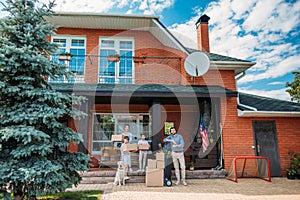 family with cardboard boxes and labrador dog standing on country house porch moving