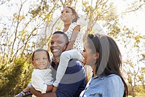 Family Carrying Children On Shoulders As They Walk In Park