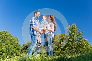 Family carrying kid, the parents standing on meadow