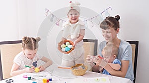 Family celebrates Easter: Mom and children paint Easter eggs at the table.