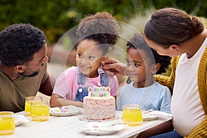 Family Celebrating Child's Birthday In Garden At Home Blowing Out Candles On Cake