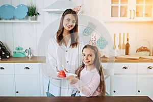 Family is celebrating little daughter`s Birthday. Attractive young woman with her charming daughter in pink clothes on kitchen.