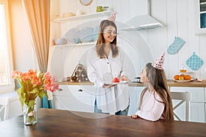 Family is celebrating little daughter`s Birthday. Attractive young woman with her charming daughter in pink clothes on kitchen.