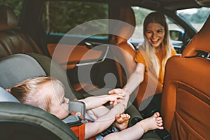 Family child in car holding mother hand baby sitting in safety seat mom driver