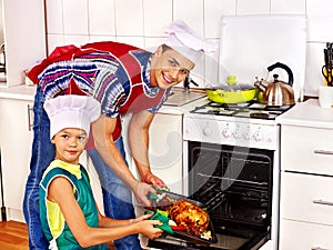 Family with child cooking chicken at kitchen.