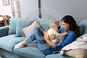 Family, child and motherhood concept - happy smiling young mother hugging little baby at home. Woman and her newborn boy or girl