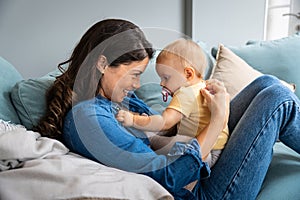 Family, child and motherhood concept - happy smiling young mother hugging little baby at home. Woman and her newborn boy or girl