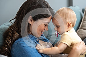 Family, child and motherhood concept - happy smiling young mother hugging little baby at home. Woman and her newborn boy or girl