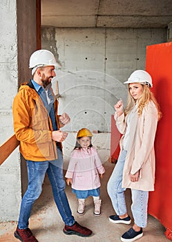 Family with child new home owners standing at construction site.