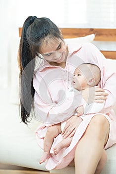 Family, child and parenthood concept - happy beautiful young asian mother smiling hugging holding newborn baby in her arms at home
