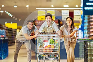 Family with child and shopping cart buying food at grocery store or supermarket