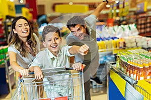 Family with child and shopping cart buying food at grocery store or supermarket