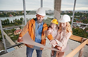 Family with child studying building plan at construction site.