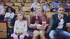 Family with child wearing protective masks eating popcorn and watching a movie in the cinema
