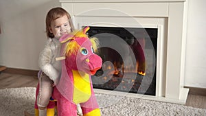 Family childhood. Happy little toddler child girl warm sweater winter clothes playing ridding on soft horse in room