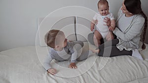 Family, childhood, infant concepts - Two children with newborn baby jumping with mom on bed. Siblings little boy and