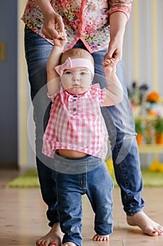 Family, childhood and parenthood concept - happy little baby learning to walk with mother help at home