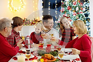 Family with children eating Christmas dinner at fireplace and decorated Xmas tree. Parents, grandparents and kids at festive meal